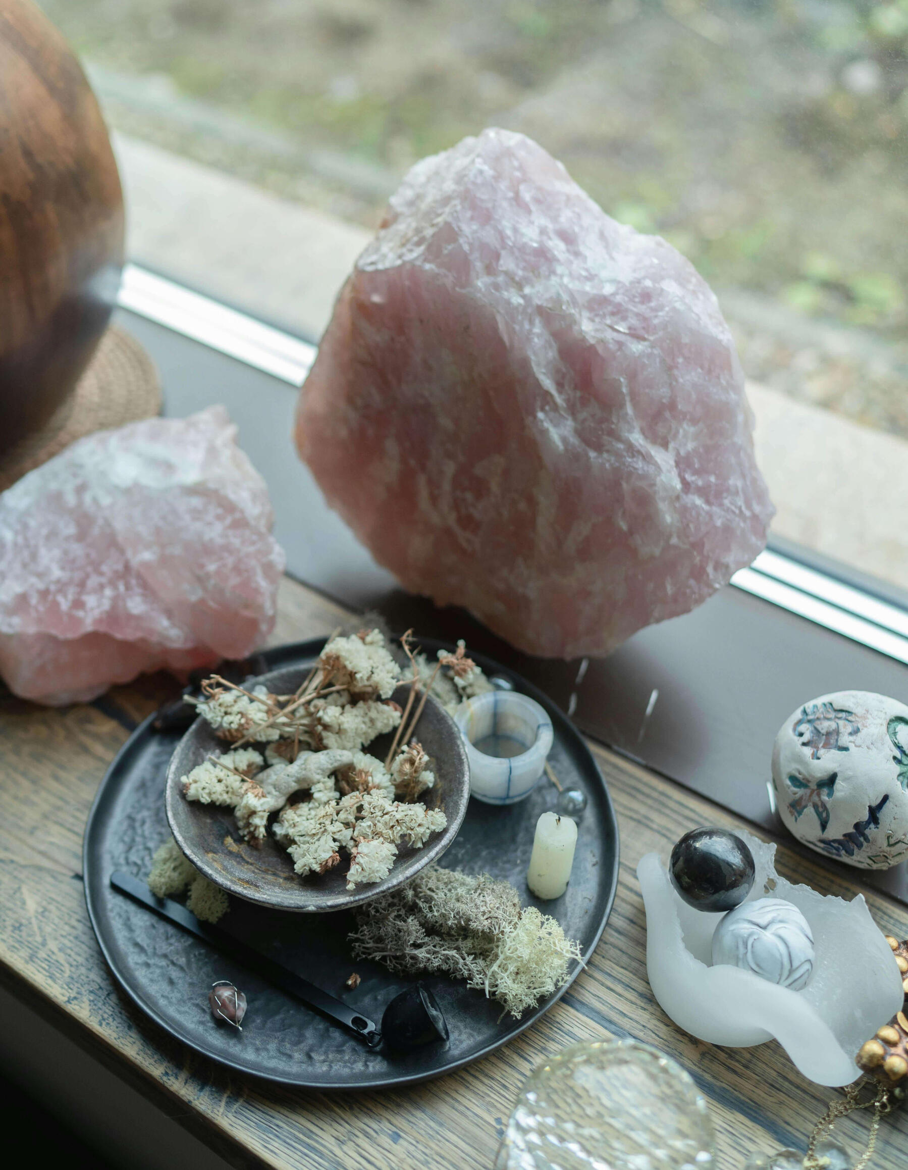 Photo of large rose quartz crystals and smaller crystals, candles and bowls of moss.